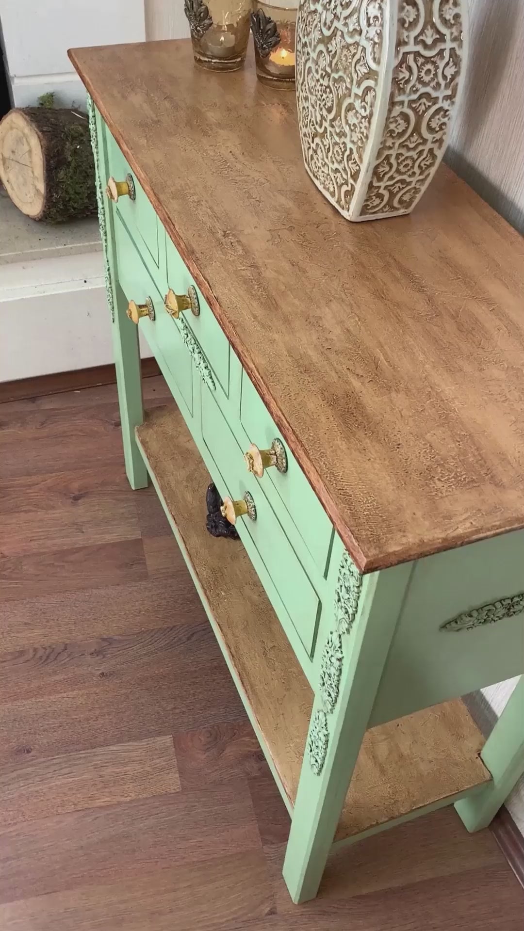 Mint yeşili boyalı, oyma detaylı çekmecelere sahip, üst kısmı ahşap kaplamalı dekoratif dresuar; üzerinde seramik vazo ve mumluklar, alt rafında dekoratif objeler bulunan vintage tarz konsol.